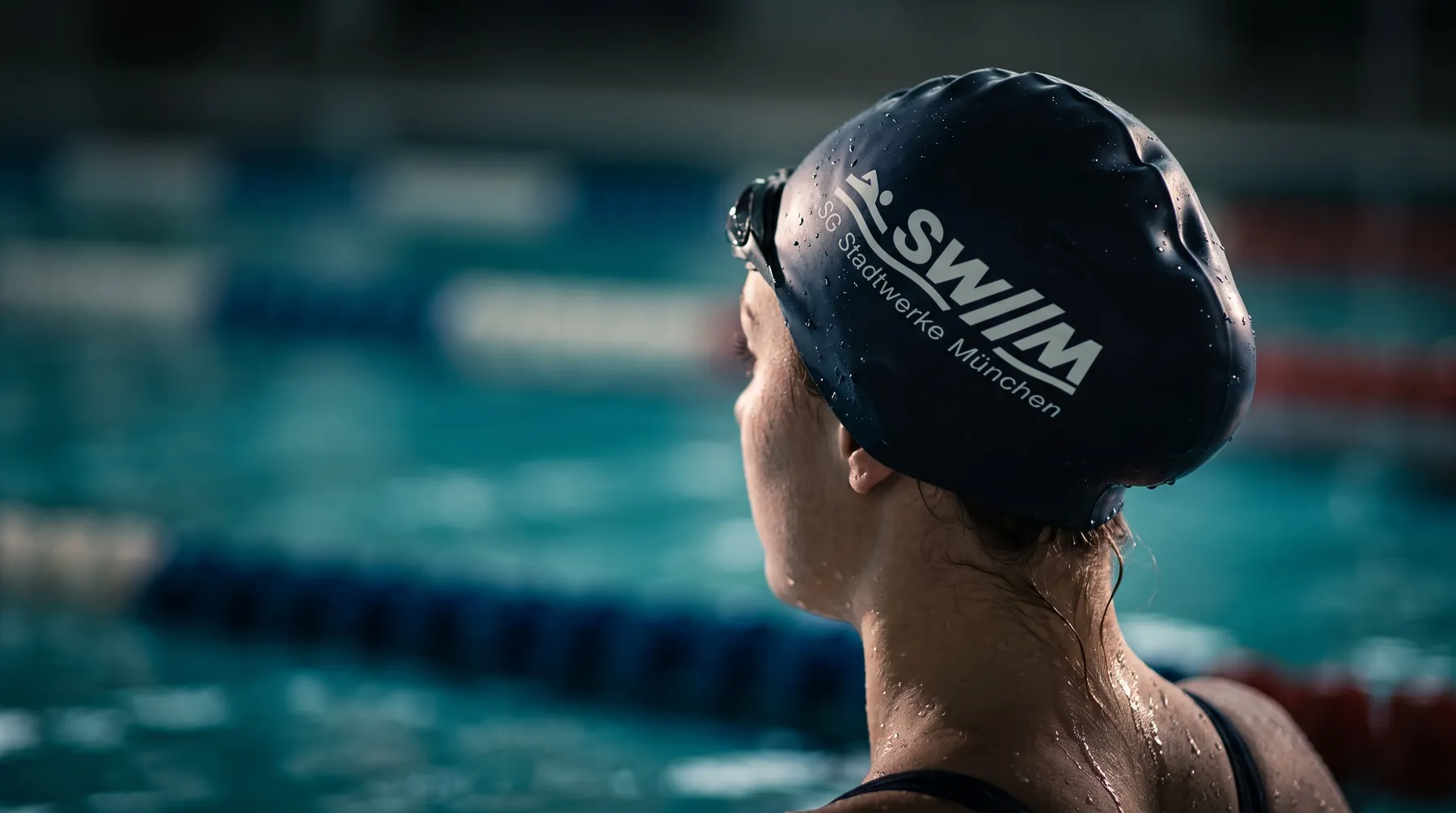 Schwimmerin von hinten mit bedruckter Vereins-Badekappe, lange Haare im Nacken